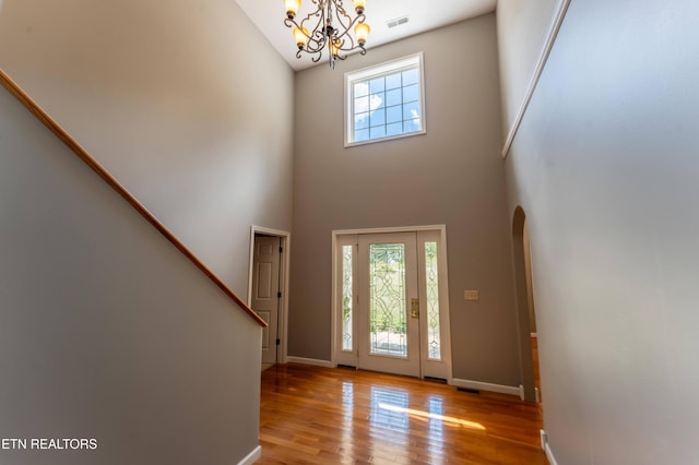 entryway with a towering ceiling, a chandelier, and light wood-type flooring