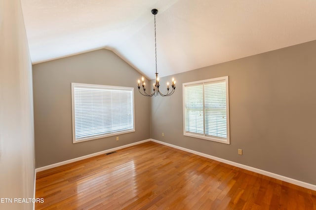 empty room with an inviting chandelier, hardwood / wood-style flooring, and vaulted ceiling