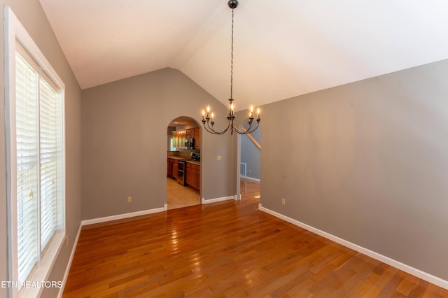 unfurnished dining area with hardwood / wood-style floors, lofted ceiling, and an inviting chandelier