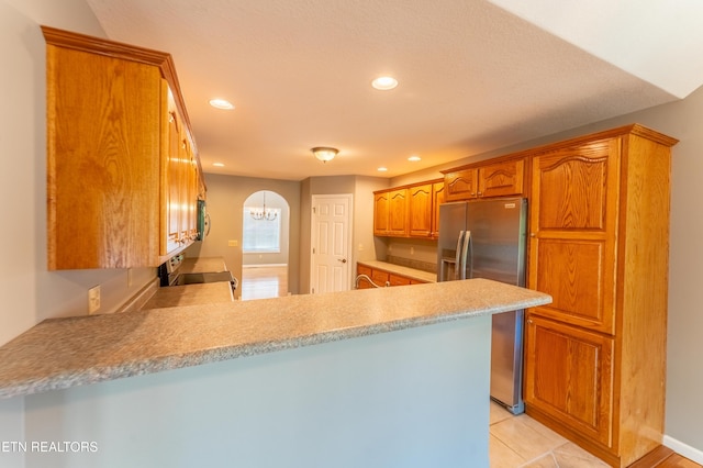 kitchen with kitchen peninsula, stainless steel fridge, light tile patterned floors, and range