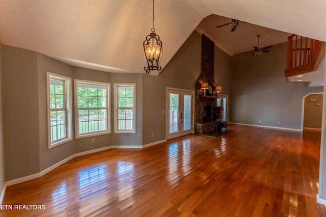 unfurnished living room with french doors, ceiling fan with notable chandelier, a fireplace, hardwood / wood-style floors, and lofted ceiling