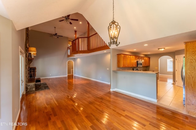 unfurnished living room featuring high vaulted ceiling, light hardwood / wood-style floors, and ceiling fan with notable chandelier