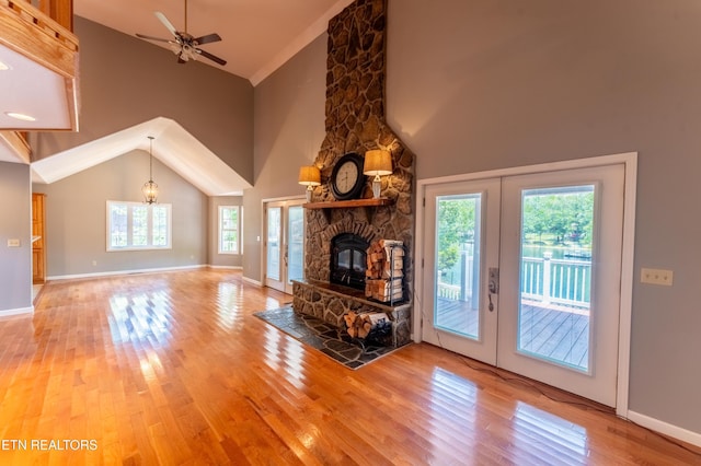 unfurnished living room featuring ceiling fan with notable chandelier, a stone fireplace, wood-type flooring, and french doors