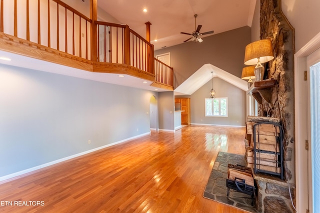 unfurnished living room featuring ceiling fan with notable chandelier, wood-type flooring, and a high ceiling