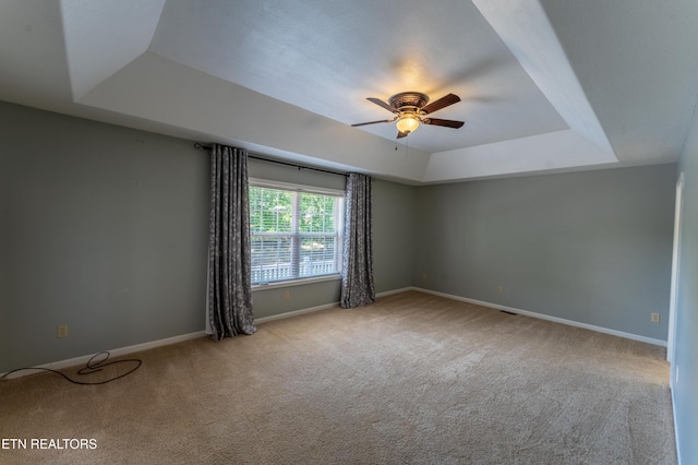 carpeted empty room featuring ceiling fan and a raised ceiling