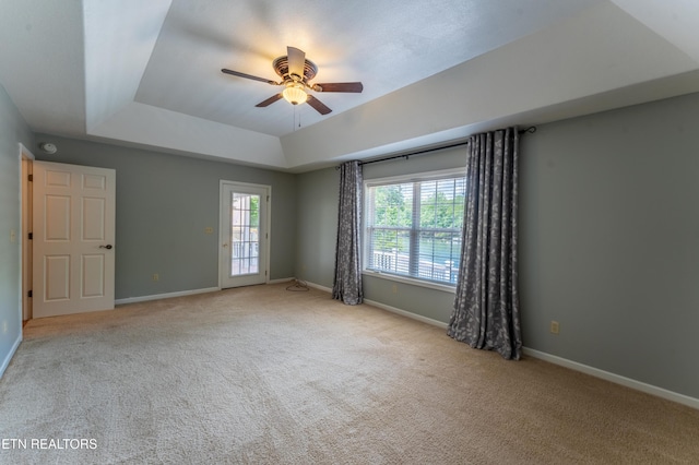 empty room with light carpet, a tray ceiling, and ceiling fan