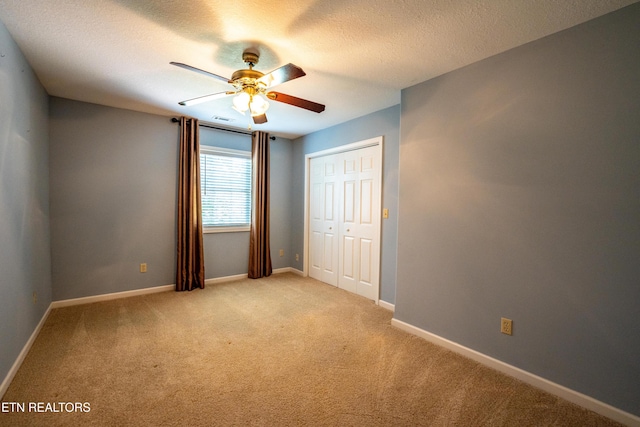 unfurnished bedroom featuring ceiling fan, a closet, light colored carpet, and a textured ceiling