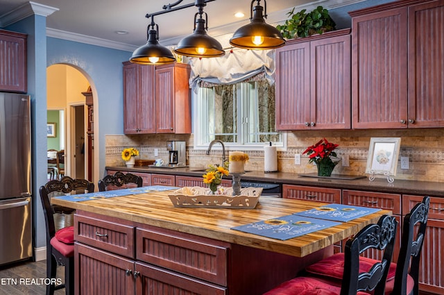 kitchen with backsplash, ornamental molding, pendant lighting, stainless steel refrigerator, and butcher block counters