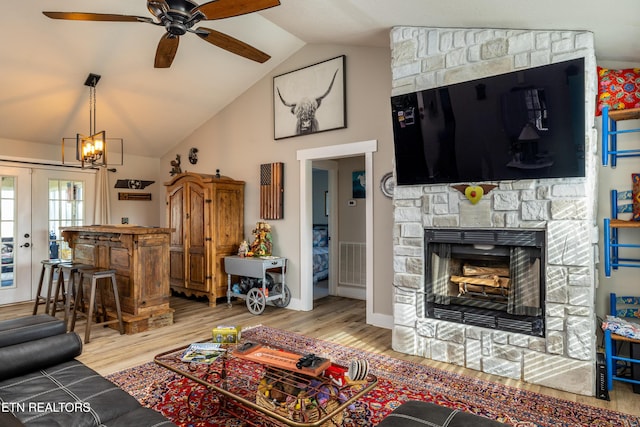 living room with a stone fireplace, lofted ceiling, light hardwood / wood-style floors, and ceiling fan with notable chandelier