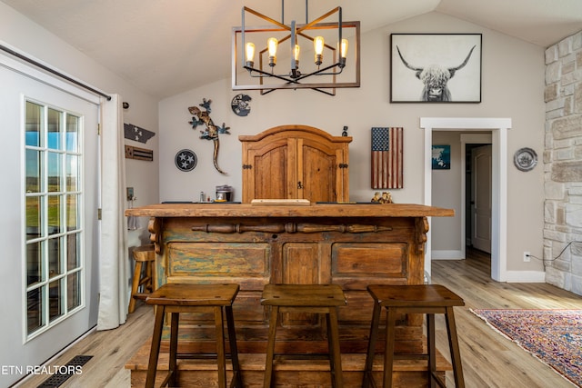 bar with pendant lighting, light hardwood / wood-style floors, vaulted ceiling, and an inviting chandelier