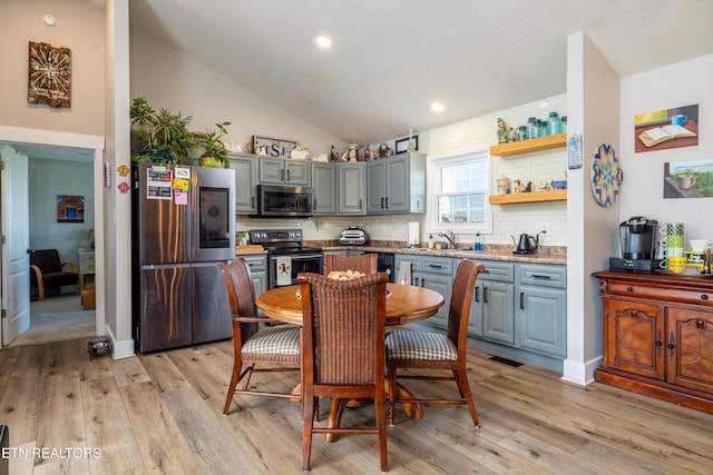 kitchen with sink, stainless steel appliances, light hardwood / wood-style flooring, backsplash, and lofted ceiling