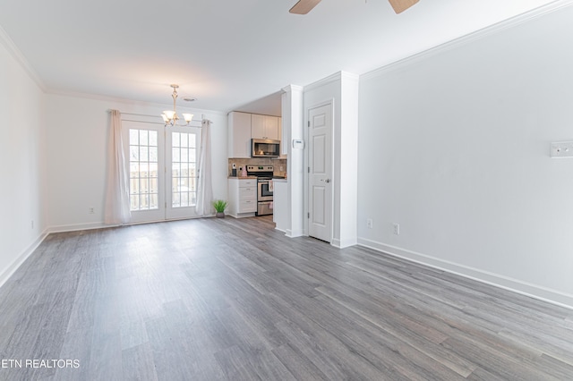 unfurnished living room featuring french doors, ceiling fan with notable chandelier, light hardwood / wood-style flooring, and crown molding