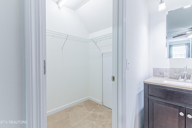 spacious closet featuring ceiling fan, sink, light colored carpet, and vaulted ceiling