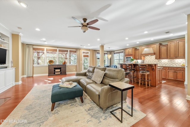 living room with crown molding, wood-type flooring, ceiling fan, and a fireplace