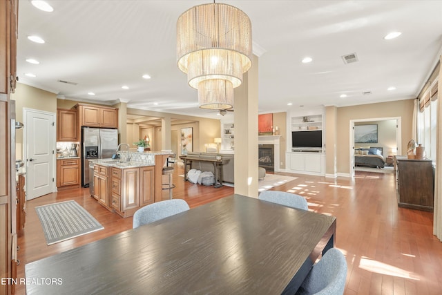 dining space featuring sink, light hardwood / wood-style flooring, ornamental molding, built in features, and a notable chandelier