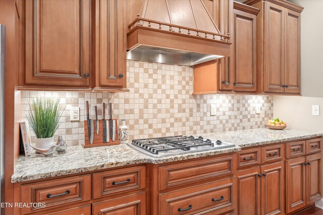 kitchen featuring tasteful backsplash, light stone countertops, stainless steel gas stovetop, and premium range hood