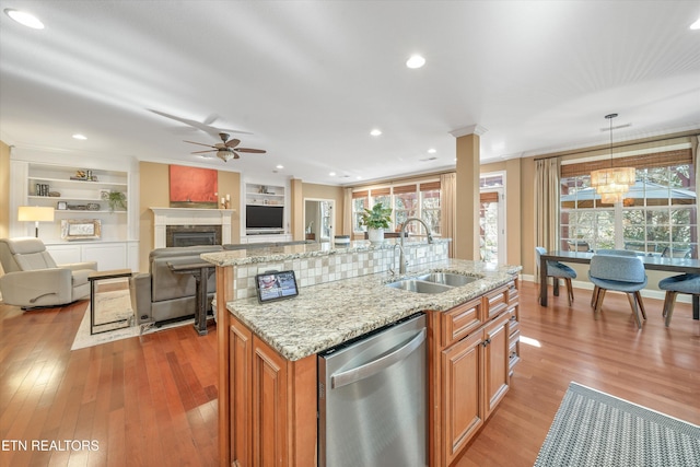 kitchen featuring sink, light stone counters, a center island with sink, dishwasher, and pendant lighting