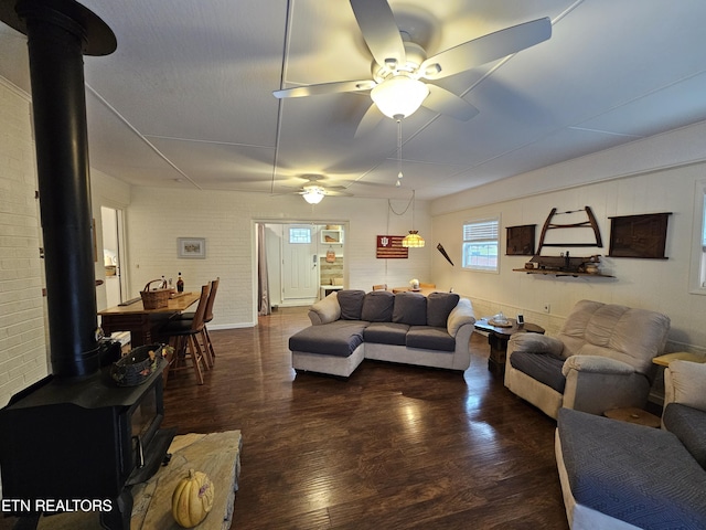 living room with a wood stove, brick wall, ceiling fan, and wood finished floors