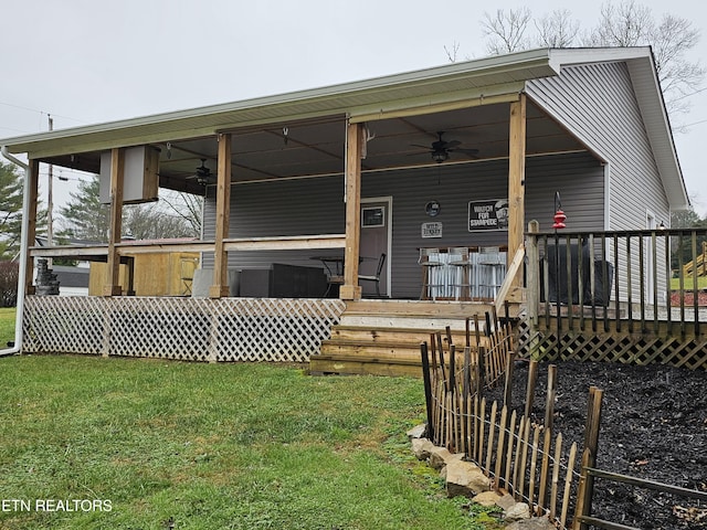 rear view of house featuring ceiling fan, a deck, a yard, and a hot tub