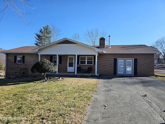 single story home with a front yard, a chimney, a porch, and brick siding