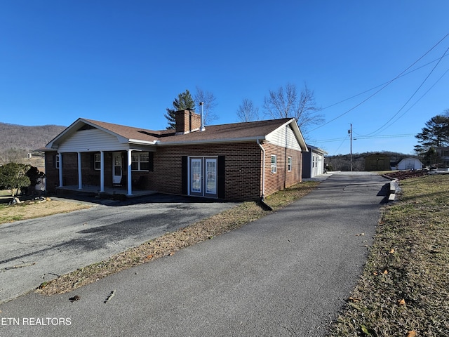 view of front facade featuring covered porch, brick siding, a chimney, and french doors