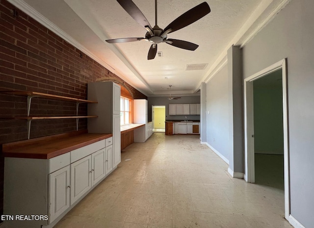 unfurnished living room with a textured ceiling, ceiling fan, and brick wall