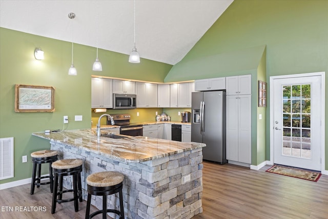 kitchen featuring kitchen peninsula, a kitchen bar, stainless steel appliances, decorative light fixtures, and white cabinetry