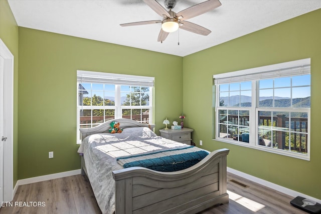 bedroom with hardwood / wood-style floors, ceiling fan, and a mountain view