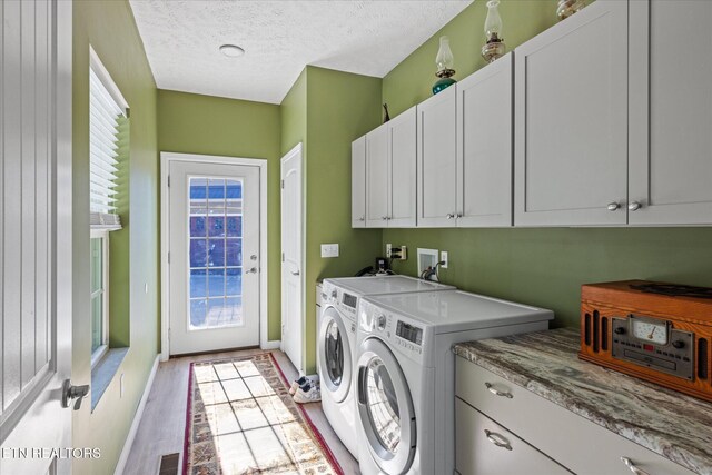 clothes washing area with washer and dryer, plenty of natural light, cabinets, and a textured ceiling