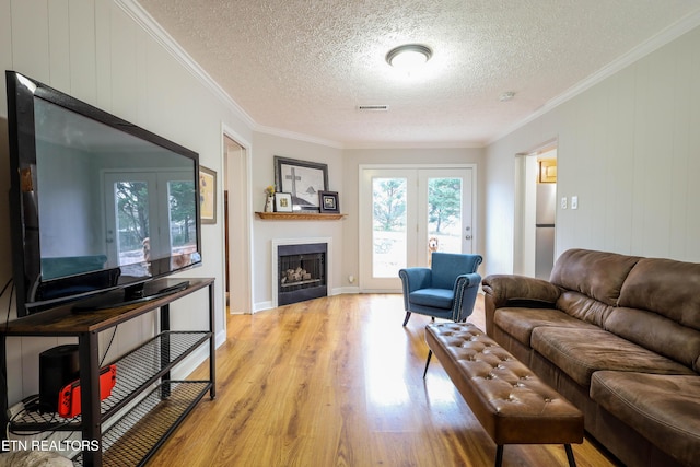 living room with french doors, a textured ceiling, light hardwood / wood-style floors, and ornamental molding