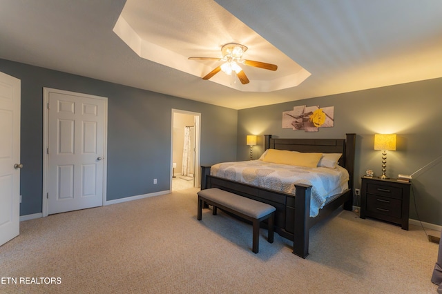 carpeted bedroom with connected bathroom, a tray ceiling, and ceiling fan