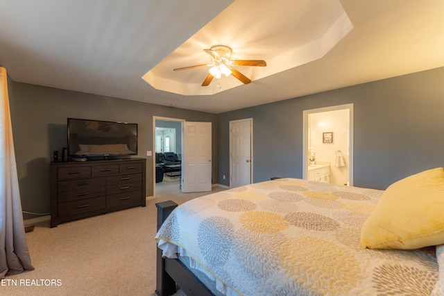 bedroom with light carpet, a tray ceiling, ensuite bath, and ceiling fan