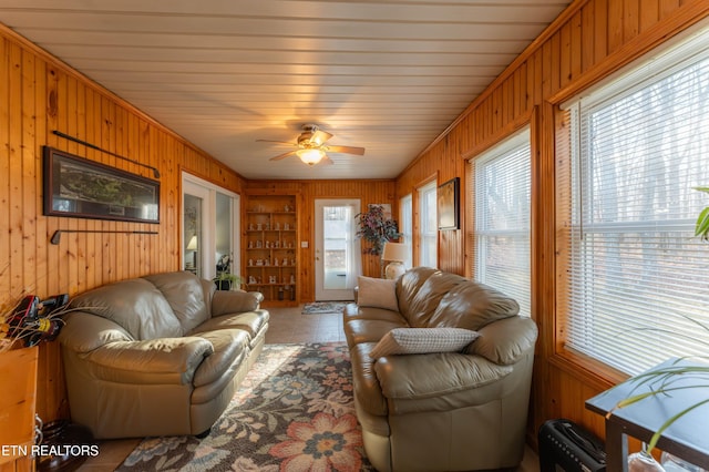 living room featuring built in shelves, ceiling fan, and wood walls