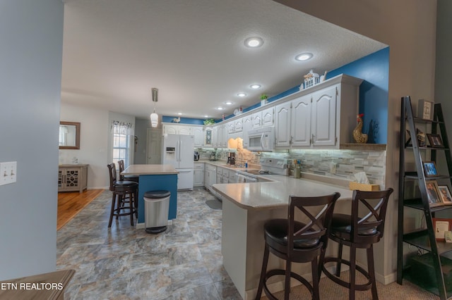 kitchen featuring a breakfast bar, white appliances, white cabinets, a kitchen island, and kitchen peninsula