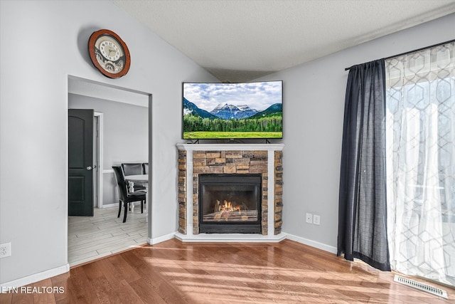 unfurnished living room featuring hardwood / wood-style flooring, a stone fireplace, vaulted ceiling, and a textured ceiling