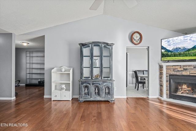 unfurnished living room featuring hardwood / wood-style flooring, vaulted ceiling, ceiling fan, and a fireplace