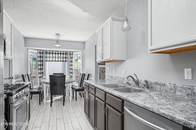 kitchen with pendant lighting, white cabinetry, sink, stainless steel appliances, and a textured ceiling