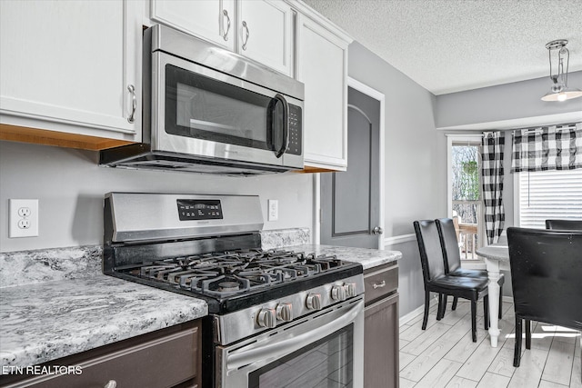 kitchen with white cabinetry, light stone counters, stainless steel appliances, a textured ceiling, and light hardwood / wood-style flooring