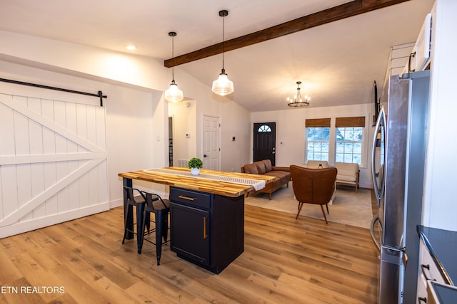 kitchen featuring a kitchen bar, stainless steel fridge, lofted ceiling with beams, light hardwood / wood-style floors, and hanging light fixtures