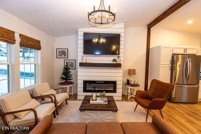 living room with vaulted ceiling with beams, a large fireplace, an inviting chandelier, and light wood-type flooring