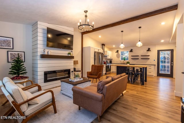 living room with vaulted ceiling with beams, light hardwood / wood-style floors, a fireplace, and an inviting chandelier