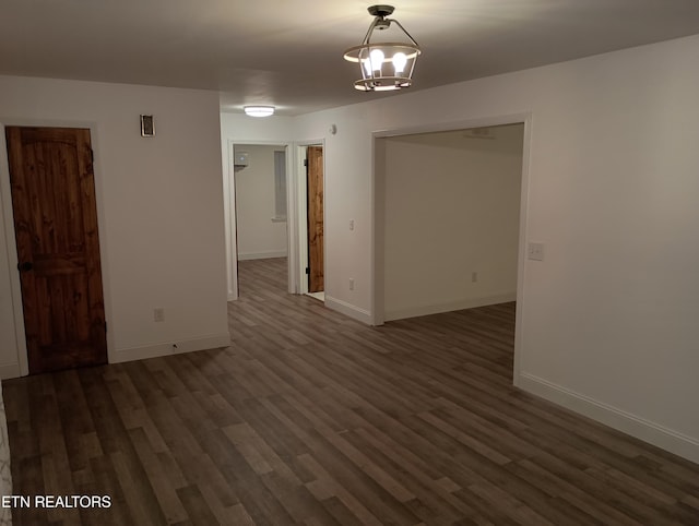 empty room with dark hardwood / wood-style flooring and a notable chandelier