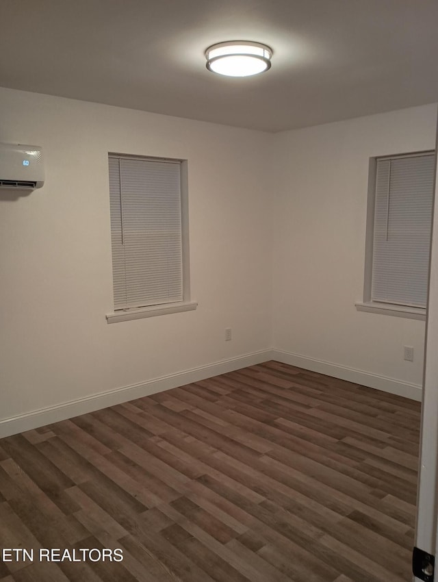 spare room with a wall unit AC and dark hardwood / wood-style floors