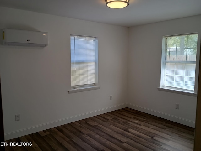 empty room featuring a wall unit AC, baseboards, and dark wood-style floors