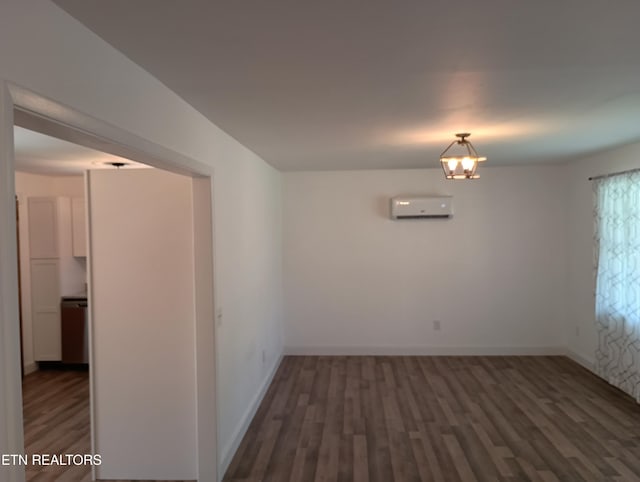 spare room featuring an inviting chandelier, an AC wall unit, baseboards, and wood finished floors