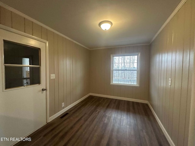 spare room with crown molding, wooden walls, and dark wood-type flooring