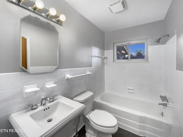 full bathroom with tiled shower / bath combo, toilet, sink, and tile walls