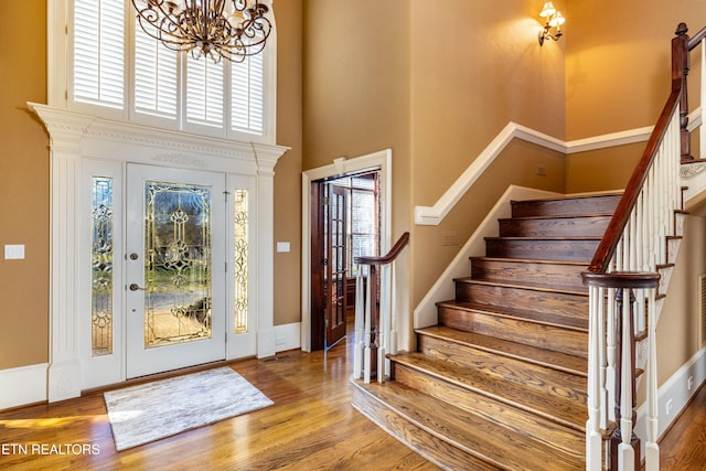 foyer with a towering ceiling, a chandelier, and light wood-type flooring