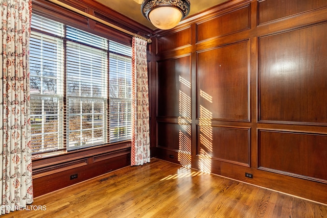 unfurnished room featuring wood-type flooring, ornamental molding, and wood walls