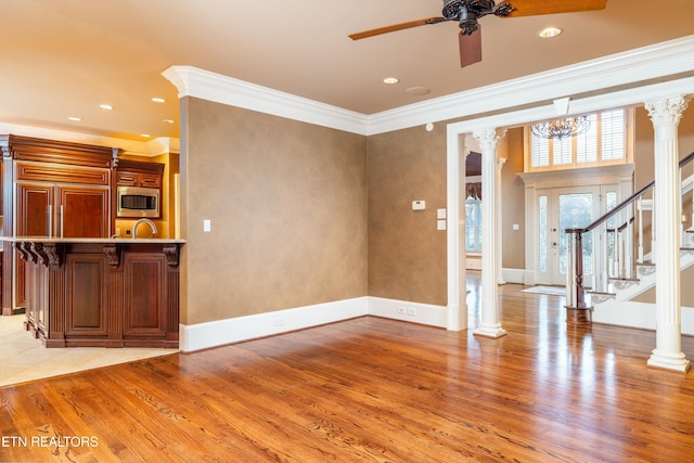 unfurnished living room featuring ceiling fan with notable chandelier, crown molding, light hardwood / wood-style flooring, and decorative columns